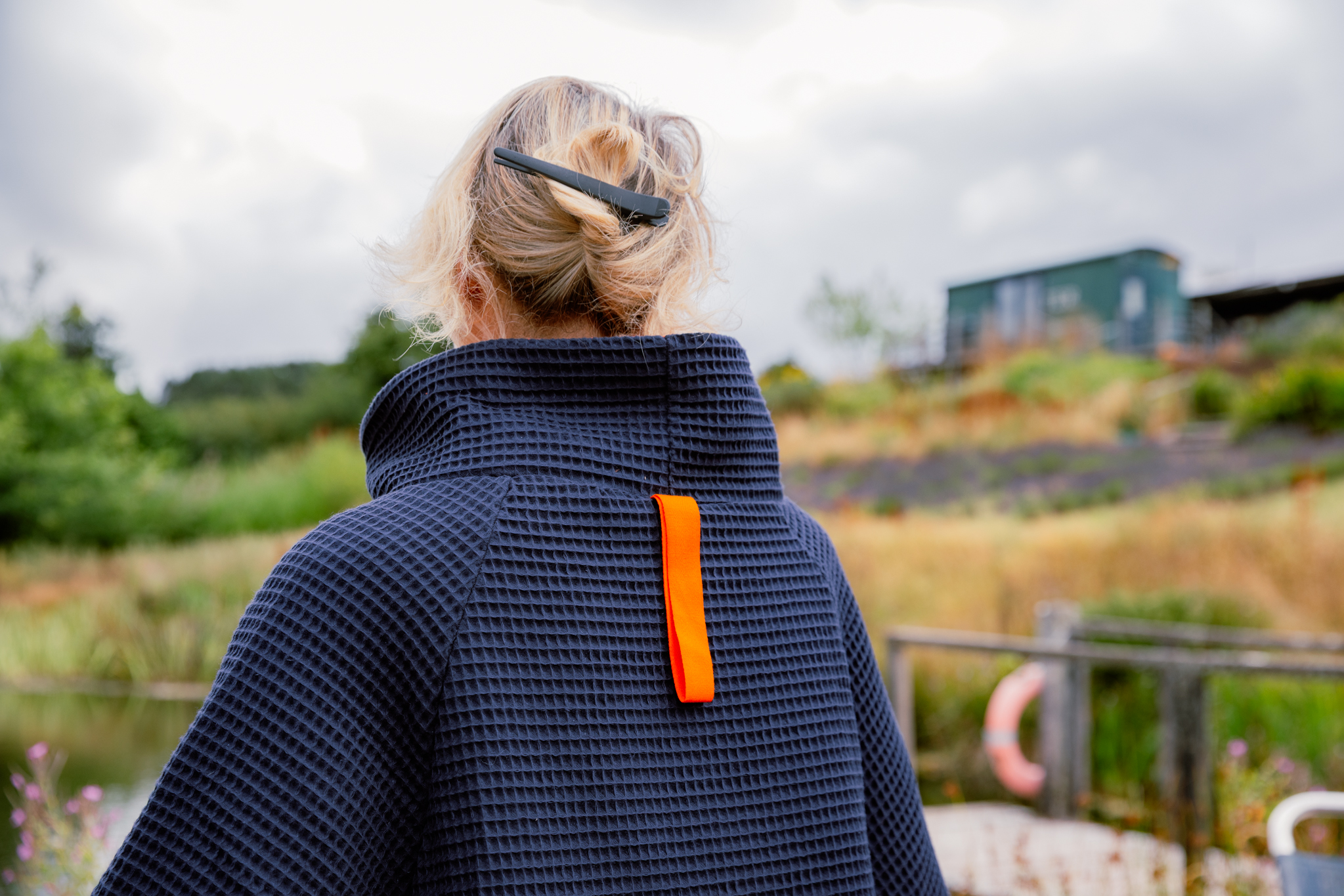Back of women wearing a navy FARMERS' Waffle robe in the countryside showing large orange loop to hang it
