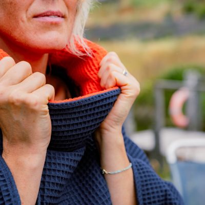 Close up of woman holding the collar of FARMERS' Waffle robe in navy, showing the orange inside of collar